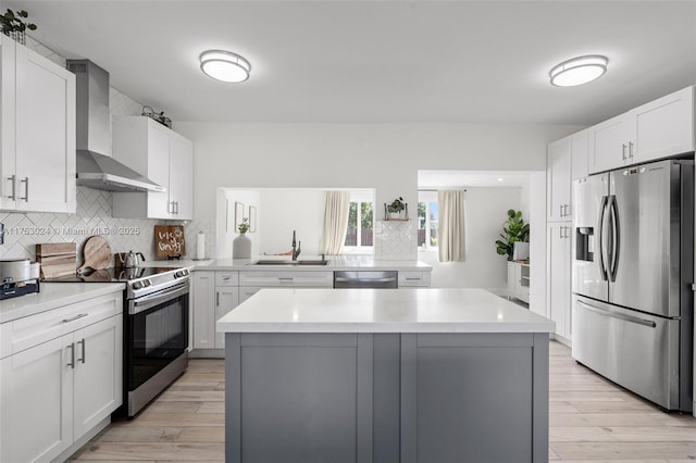 kitchen featuring a kitchen island, a sink, light countertops, appliances with stainless steel finishes, and wall chimney exhaust hood