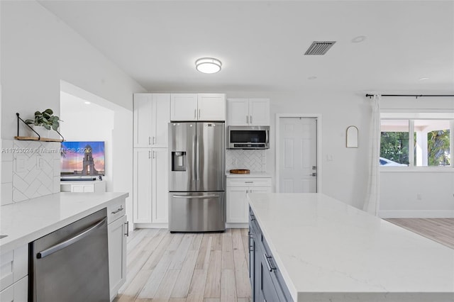 kitchen featuring decorative backsplash, appliances with stainless steel finishes, white cabinetry, light stone countertops, and light wood-type flooring