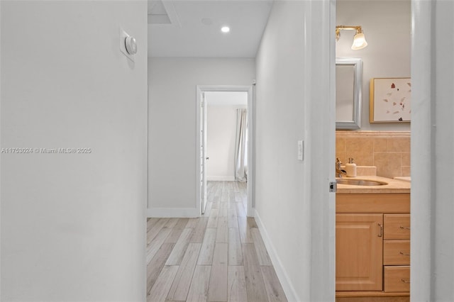 hallway featuring light wood-style floors, baseboards, a sink, and recessed lighting