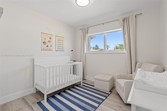 bedroom featuring a crib, wood finished floors, and baseboards