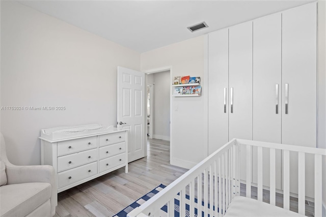 bedroom with light wood-type flooring, visible vents, and a crib