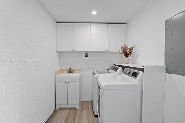 laundry room with cabinet space, electric panel, washing machine and clothes dryer, light wood-type flooring, and a sink