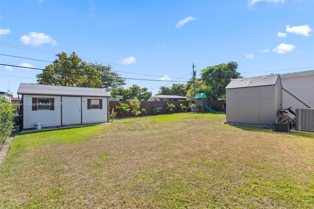 view of yard with central air condition unit, fence, a playground, and an outbuilding