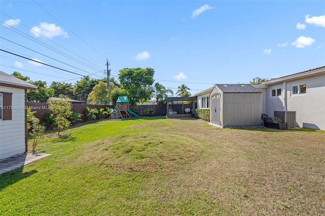 view of yard featuring an outbuilding, a playground, a fenced backyard, a storage shed, and central AC