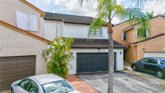 townhome / multi-family property with driveway, a tile roof, an attached garage, and stucco siding