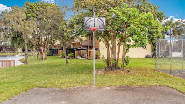 view of basketball court featuring basketball court, a water view, and a lawn