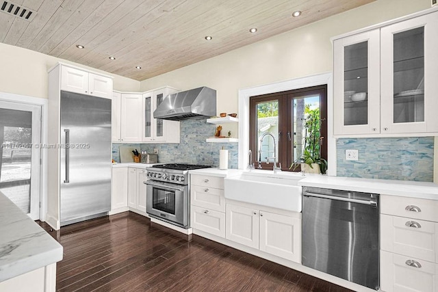 kitchen with visible vents, white cabinets, wall chimney exhaust hood, high end appliances, and glass insert cabinets