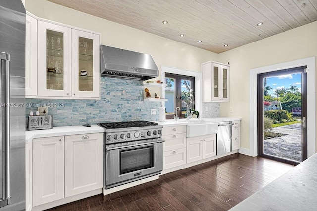 kitchen featuring stainless steel appliances, wall chimney range hood, light countertops, and glass insert cabinets