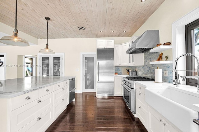 kitchen with premium appliances, decorative light fixtures, white cabinets, a sink, and wall chimney exhaust hood