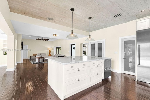 kitchen featuring light stone counters, built in refrigerator, white cabinetry, open floor plan, and decorative light fixtures