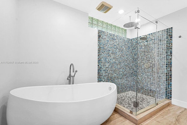 full bath with a stall shower, a freestanding tub, and wood finished floors