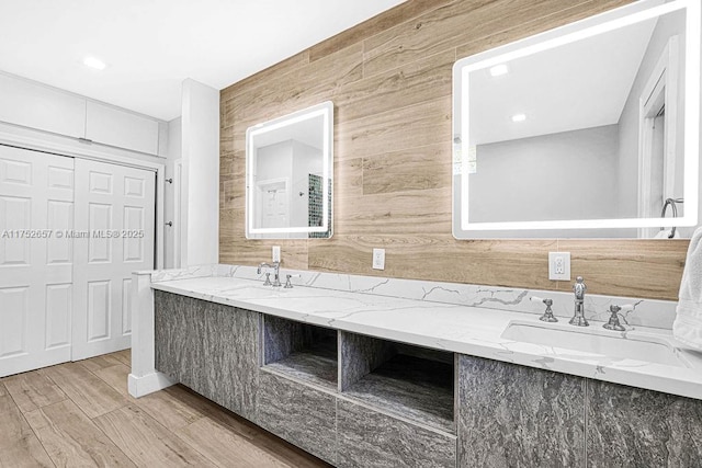 bathroom featuring double vanity, wood finished floors, wood walls, and a sink