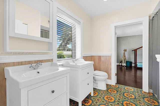 full bathroom featuring two vanities, wainscoting, a sink, and toilet