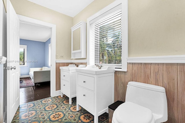 half bath with a wainscoted wall, toilet, wood walls, vanity, and wood finished floors