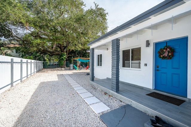 property entrance with fence, a wooden deck, and stucco siding