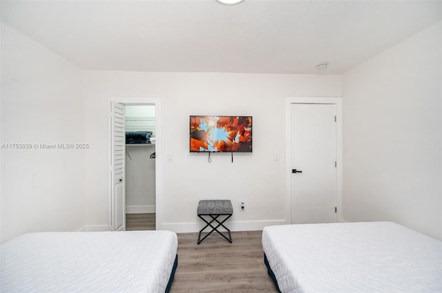 bedroom featuring a walk in closet, baseboards, and wood finished floors