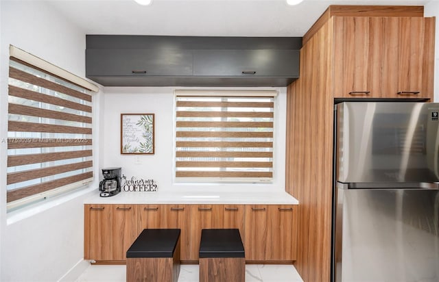 kitchen with modern cabinets, brown cabinetry, light countertops, and freestanding refrigerator