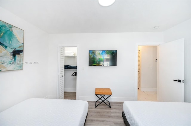 bedroom featuring light wood-type flooring, a spacious closet, and baseboards