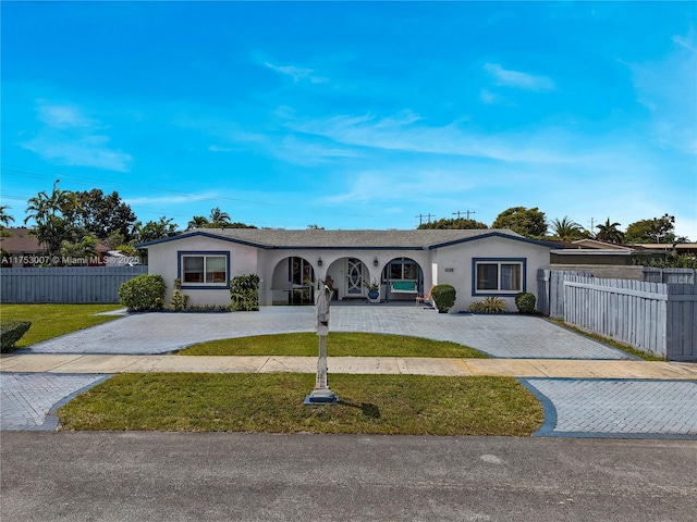 ranch-style home with a front lawn, decorative driveway, a fenced front yard, and stucco siding