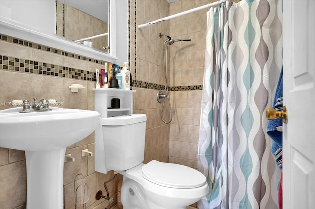 bathroom with toilet, a sink, a tile shower, and tile walls