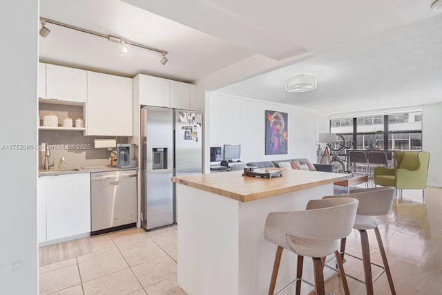 kitchen with appliances with stainless steel finishes, a kitchen breakfast bar, white cabinetry, open shelves, and a sink