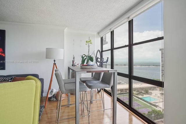 dining room featuring a textured ceiling, a water view, wood finished floors, and floor to ceiling windows