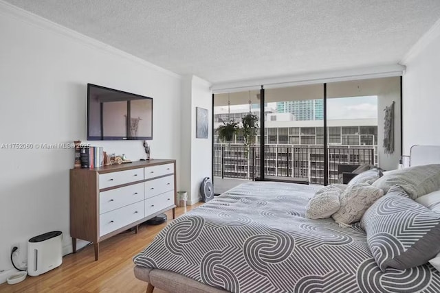 bedroom featuring access to exterior, light wood-type flooring, crown molding, and a wall of windows