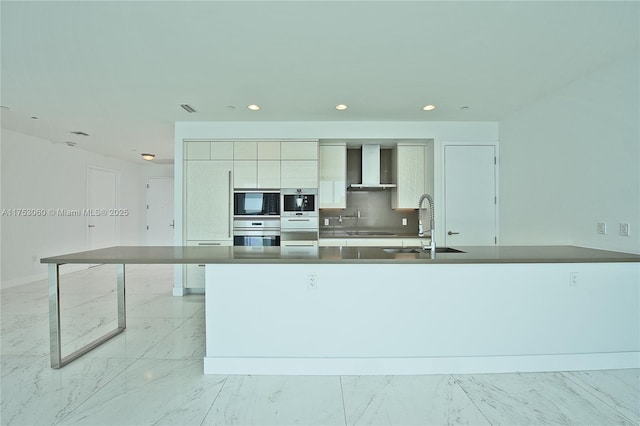 kitchen featuring marble finish floor, wall chimney range hood, modern cabinets, and a sink