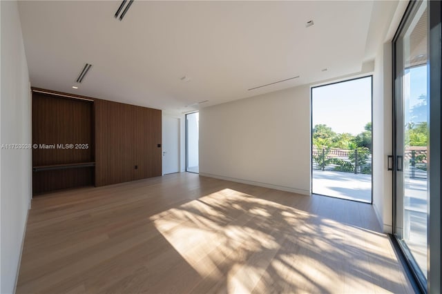 unfurnished room with expansive windows, light wood-type flooring, visible vents, and wooden walls