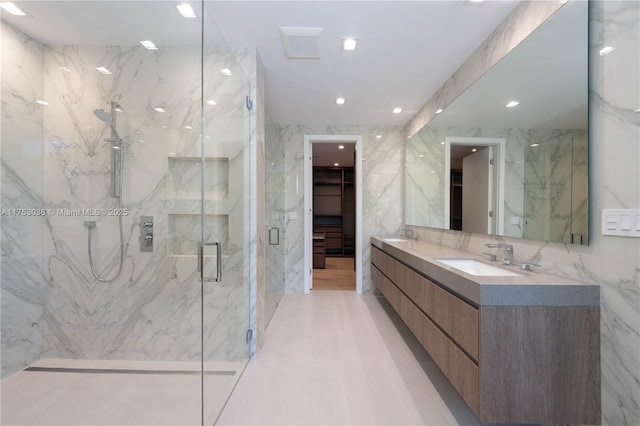 full bathroom featuring tile walls, a marble finish shower, double vanity, a spacious closet, and a sink