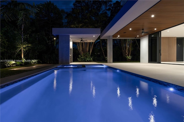 pool at night with ceiling fan, a patio area, an outdoor structure, and an outdoor pool