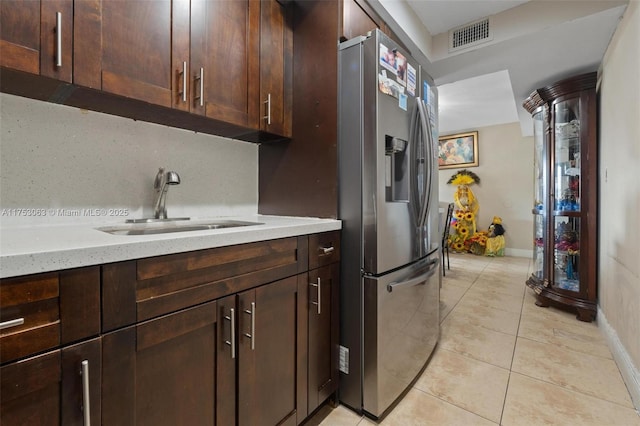 kitchen with light tile patterned floors, stainless steel fridge with ice dispenser, light stone countertops, dark brown cabinets, and a sink