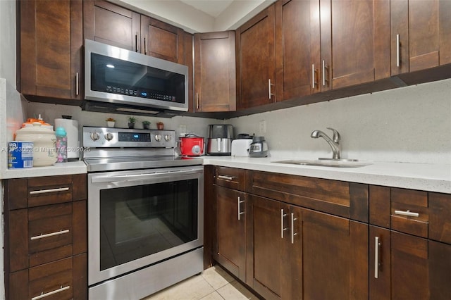 kitchen with light tile patterned flooring, dark brown cabinetry, a sink, appliances with stainless steel finishes, and light stone countertops