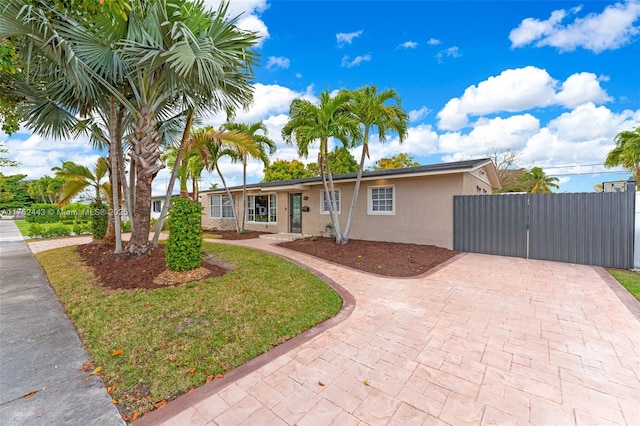 single story home with a front yard, a gate, decorative driveway, and stucco siding