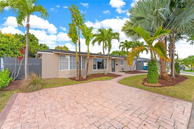 ranch-style home with a front yard, fence, decorative driveway, and stucco siding