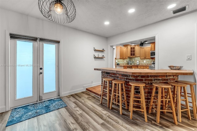 bar featuring light wood-style flooring, stainless steel appliances, visible vents, french doors, and backsplash