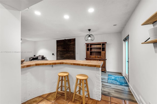 kitchen with a breakfast bar, a peninsula, pendant lighting, wooden counters, and recessed lighting