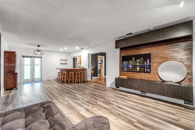 living room featuring baseboards, a bar, a textured ceiling, french doors, and light wood-type flooring