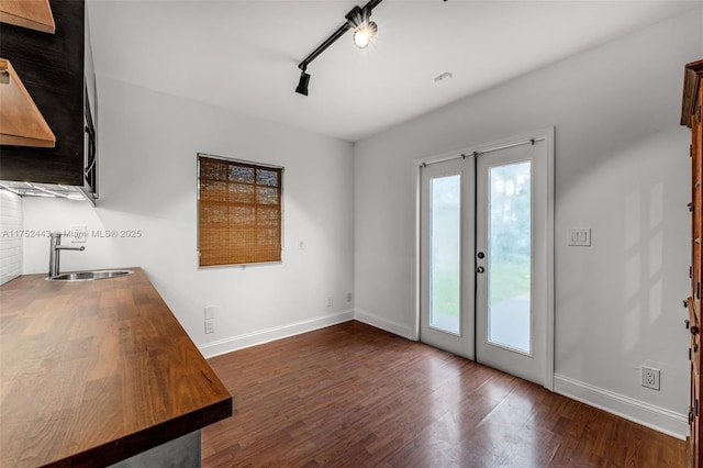 interior space featuring rail lighting, baseboards, dark wood-type flooring, and french doors