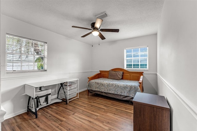 bedroom with a textured ceiling, ceiling fan, wood finished floors, visible vents, and baseboards