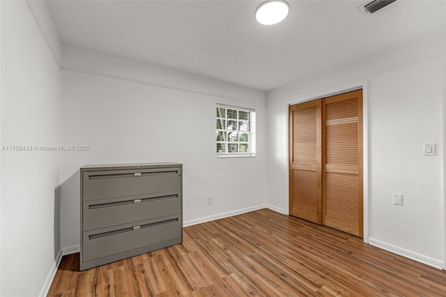 unfurnished bedroom featuring baseboards, a closet, visible vents, and light wood-style floors