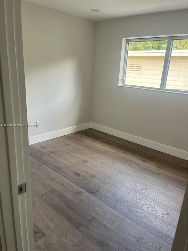 spare room with baseboards and wood finished floors