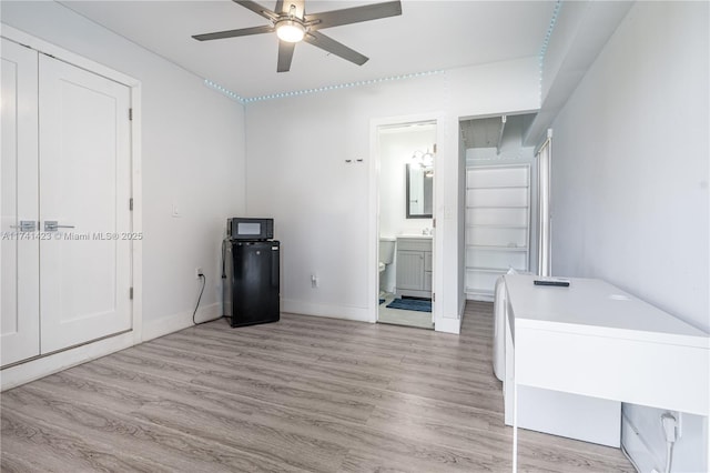 interior space featuring ensuite bathroom, light wood-style floors, a sink, ceiling fan, and baseboards