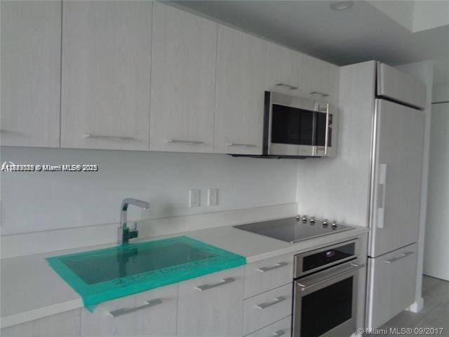 kitchen with appliances with stainless steel finishes, white cabinets, a sink, and light countertops