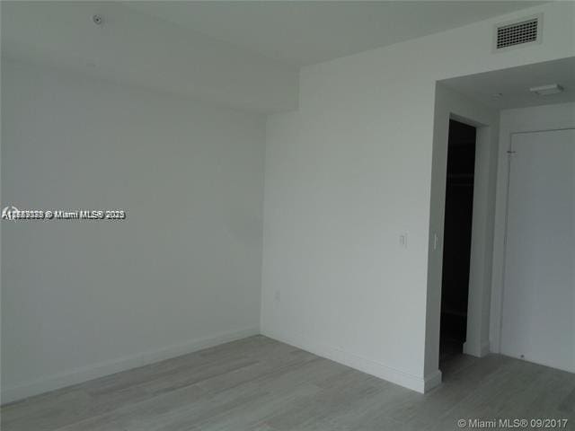 empty room with light wood-style floors, visible vents, and baseboards