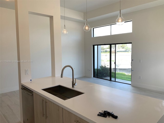 kitchen featuring a sink, light countertops, hanging light fixtures, and dishwasher