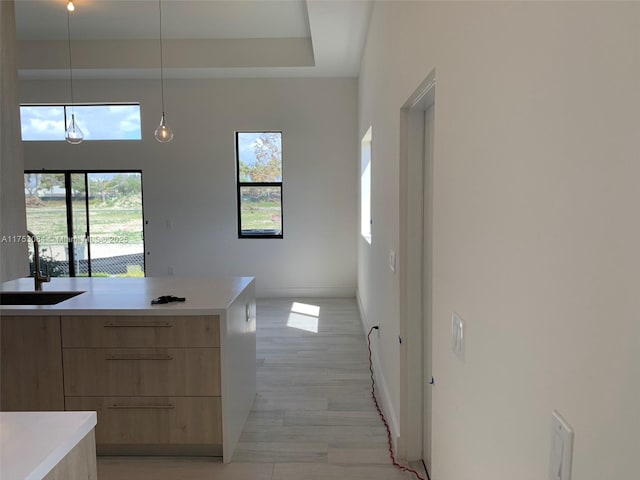 kitchen featuring light brown cabinetry, modern cabinets, light countertops, a sink, and decorative light fixtures