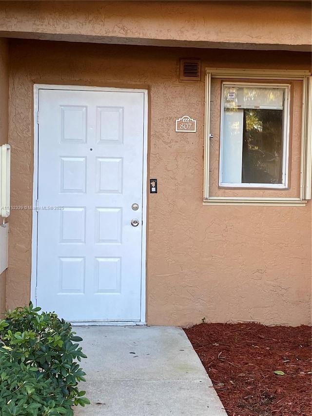 doorway to property featuring visible vents and stucco siding