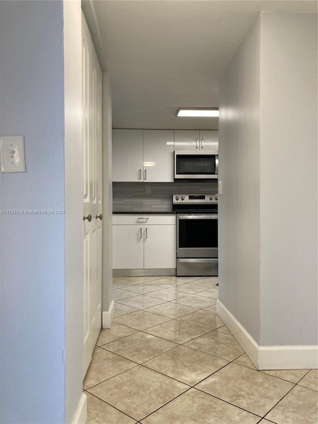 kitchen featuring light tile patterned flooring, baseboards, white cabinets, appliances with stainless steel finishes, and dark countertops