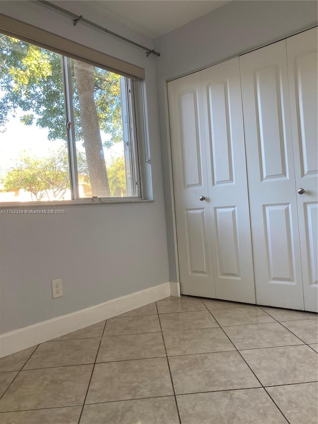 unfurnished bedroom featuring light tile patterned floors, a closet, and baseboards